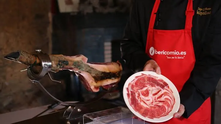 Maestro jamonero cortando jamón ibérico con delantal de Ibericomio